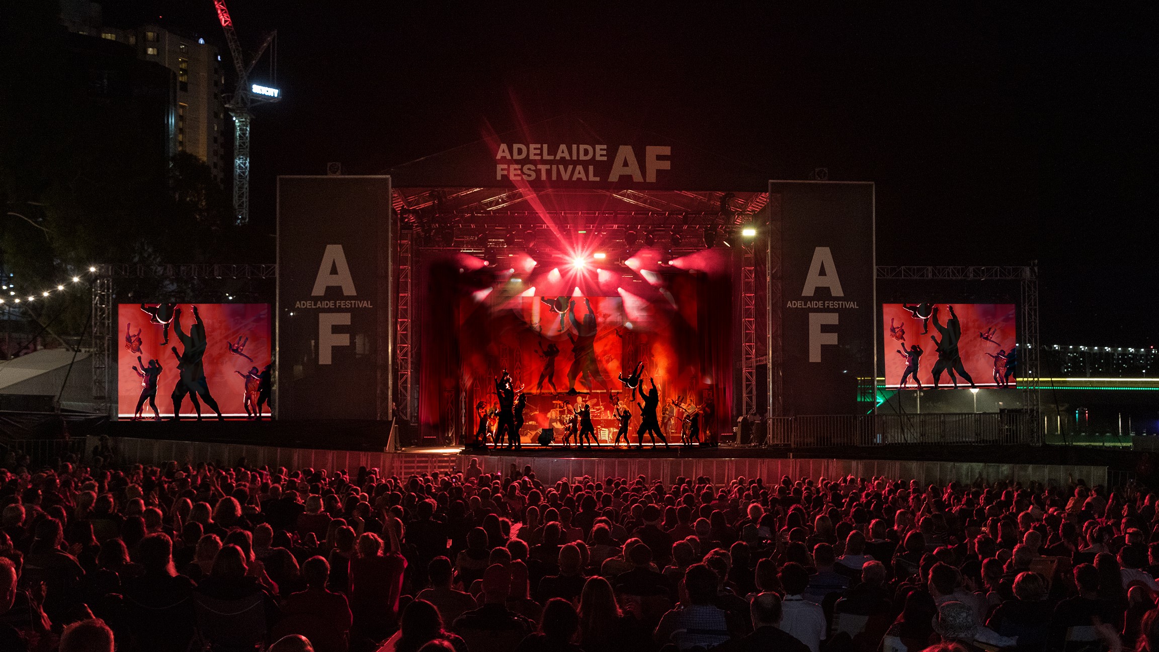 A group of people perform acrobatic moves on a large stage with Adelaide Festival branding in front of a large crowd.