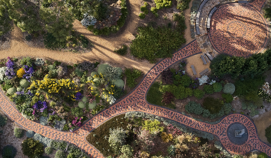 An overhead shot of the beautiful gardens at UKARIA Cultural Centre, including winding red brick paths, greenery, and flowers in shades of purple and yellow.