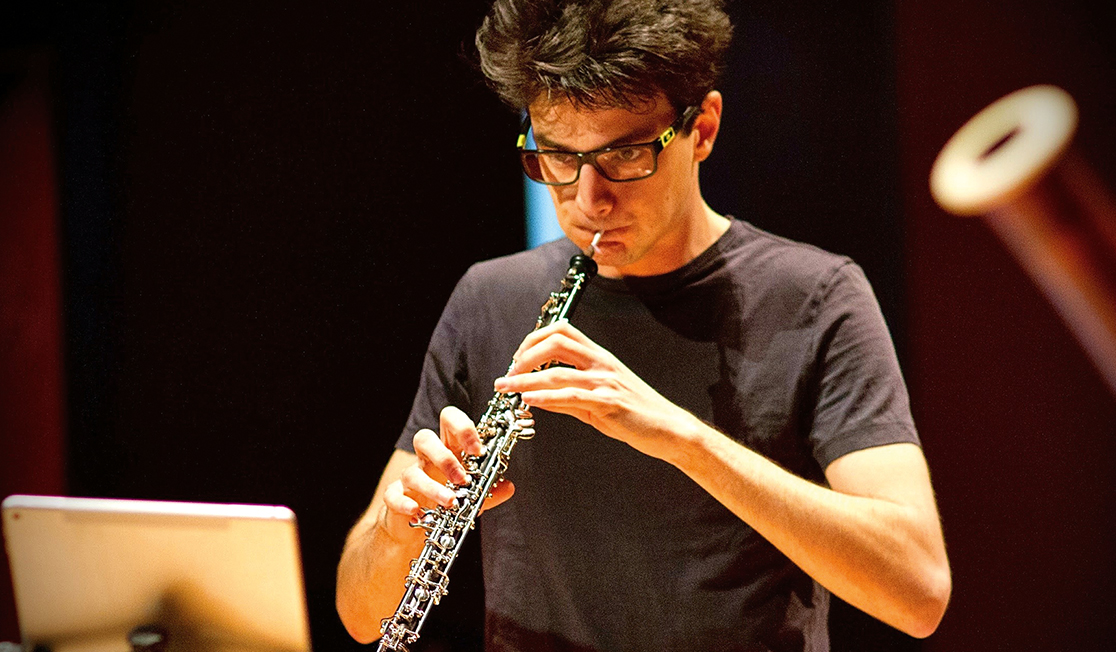 Emmanuel Cassimatis, a man with glasses, dark hair and a black t-shirt, is pictured playing the oboe.