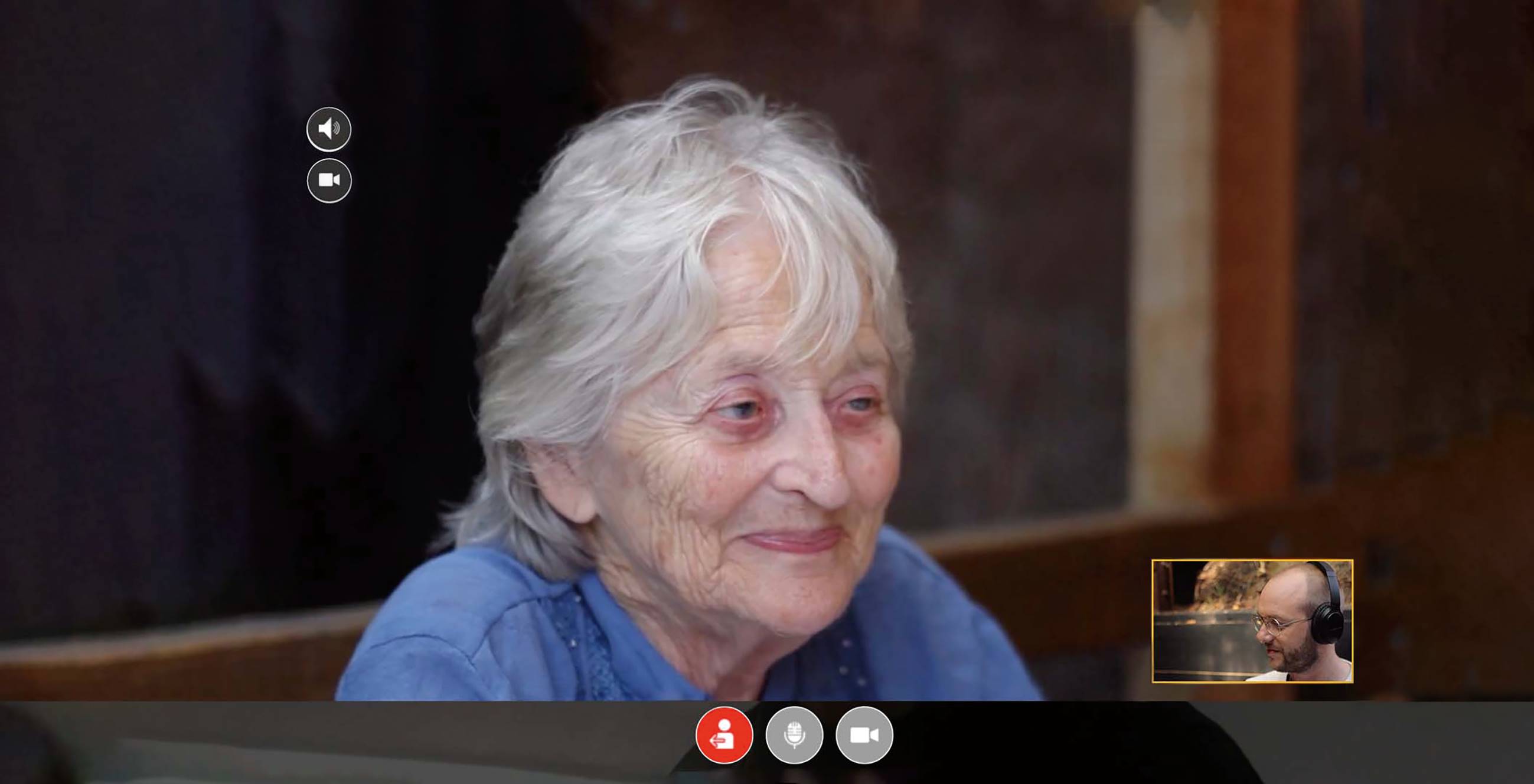 Smiling older woman pictured on a video chat with a young man wearing headphones.