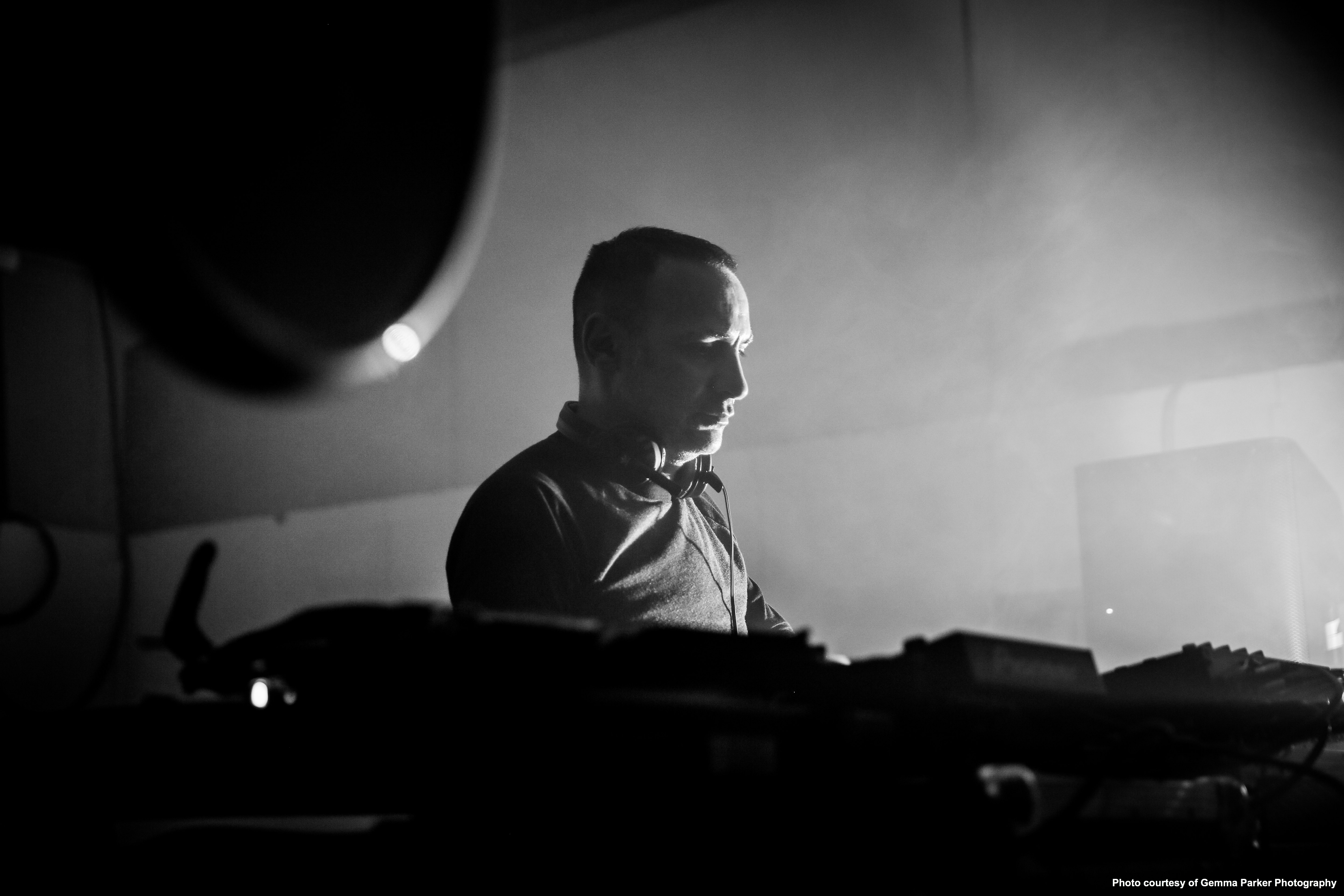 A black and white photo of a man behind a DJ deck with fog in the background.