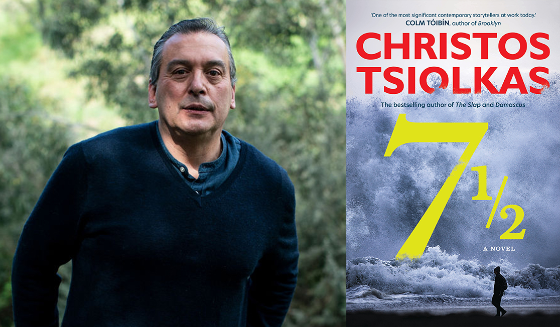 Christos Tsiolkas stands outdoors, he wears a blue knitted jumper over a blue shirt, he has short hair and is smiling